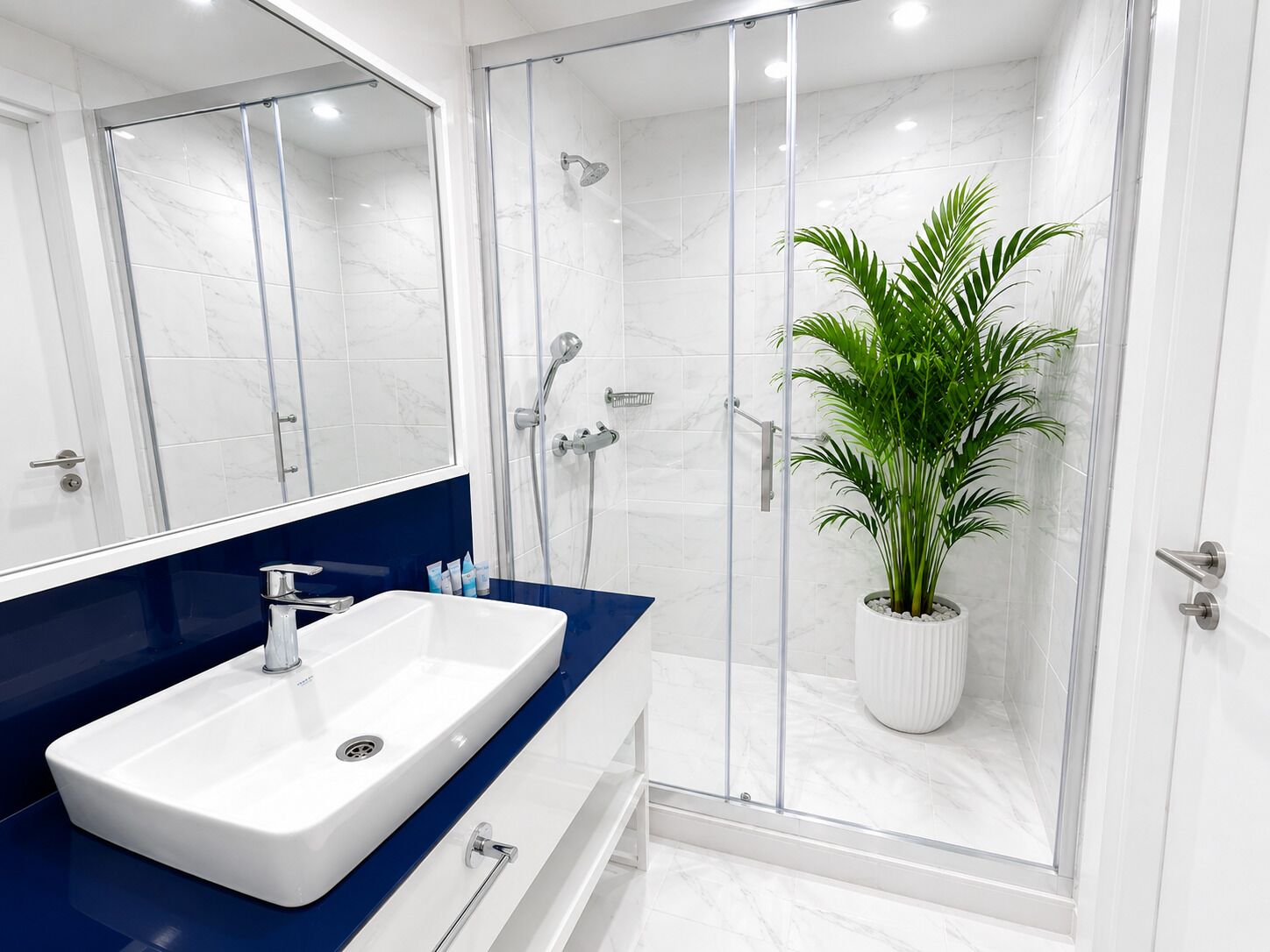 Une salle de bain moderne avec un lavabo blanc, un plan de toilette bleu et une douche séparée par une paroi de verre.