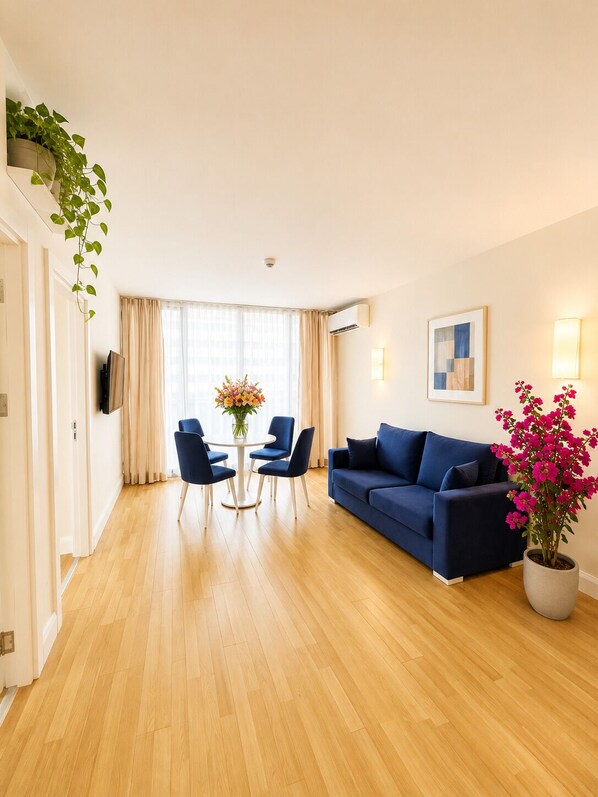 A modern living room with a blue sofa, a dining table with chairs, a potted plant, and a painting on the wall. - Orbi City Sea View (Batumi)
