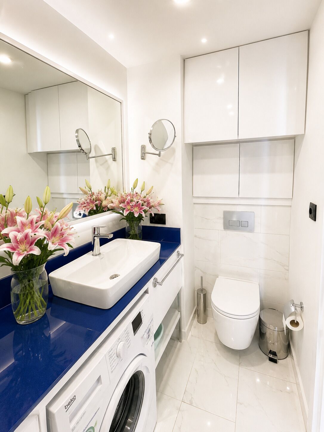 A modern bathroom with a white sink, blue countertop, and a washing machine.