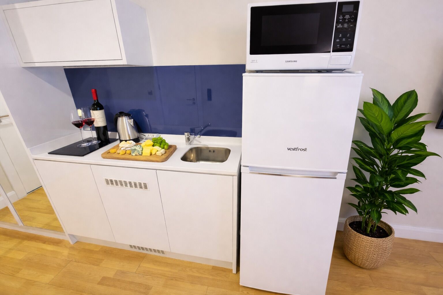 Une petite cuisine équipée d’un four à micro-ondes, d’un évier et d’un petit plan de travail sur lequel se trouvent des aliments et un verre à vin.
