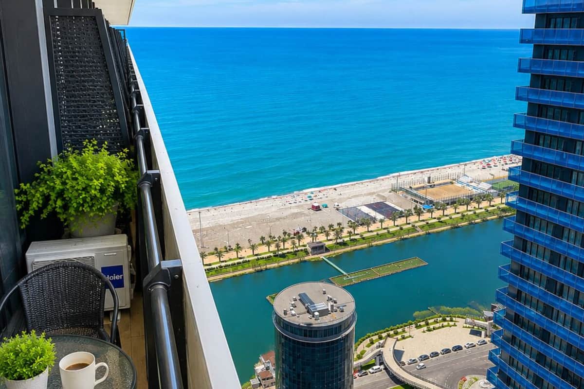 Un balcon avec vue sur la mer, un immeuble de grande hauteur et un espace de stationnement.