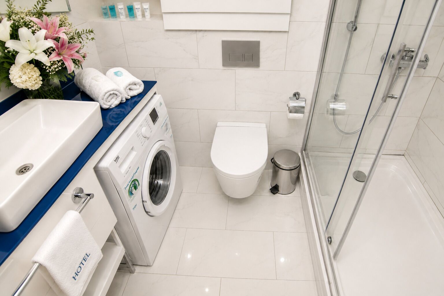 A modern bathroom with a washing machine, toilet, and glass-enclosed shower.