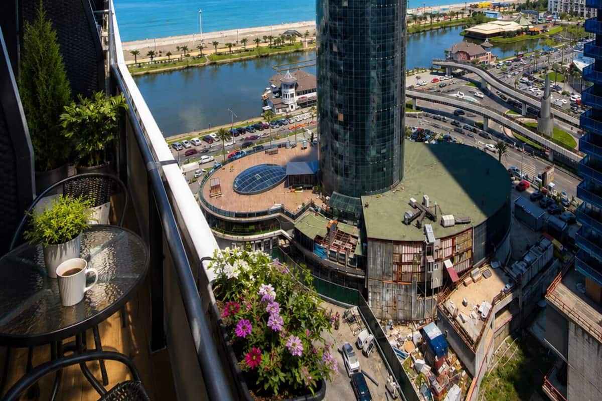 Un immeuble de grande hauteur, doté d’une façade en verre, qui offre une vue sur le paysage urbain côtier, notamment sur un port de plaisance et une plage.