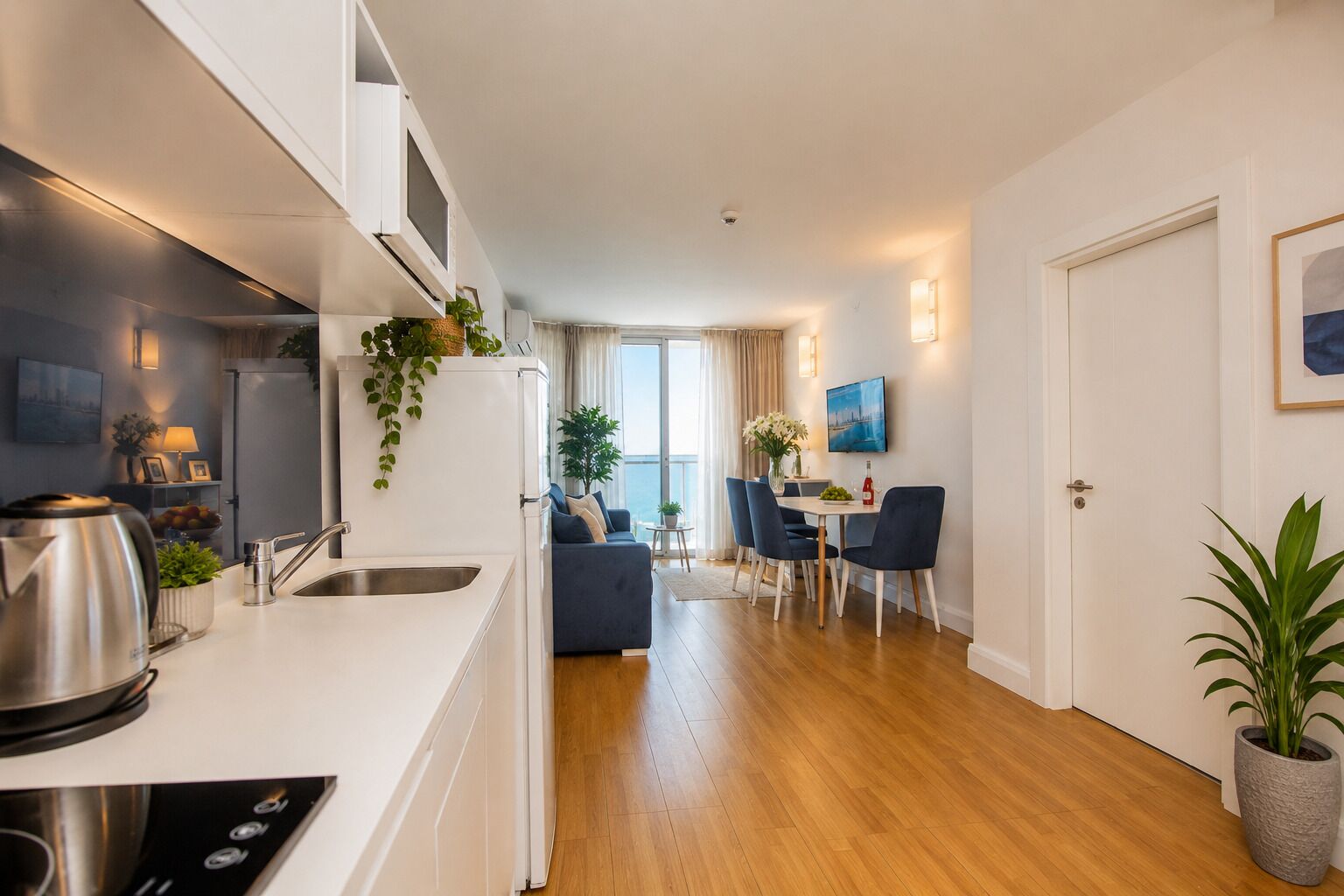 Une cuisine moderne dotée d’un four encastré, un coin repas avec une table et des chaises, et une vue sur la mer grâce à de grandes fenêtres.