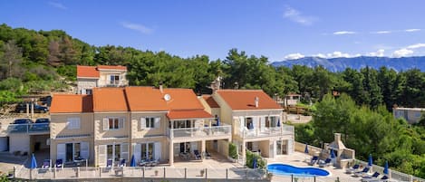 A multi-story building with a swimming pool, outdoor seating, and a view of mountains.