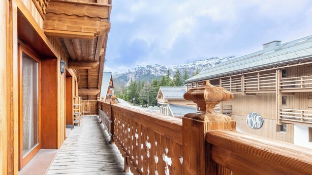Un balcon en bois offrant une vue sur des montagnes enneigées et un bâtiment traditionnel.