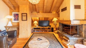 Un salon chaleureux avec des poutres en bois, une cheminée, un téléviseur et un coin salon confortable.