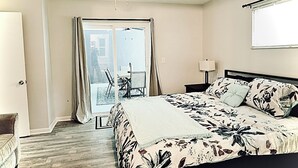 Une chambre à coucher comprenant un lit, une table de chevet, une lampe, une chaise et une porte-fenêtre coulissante donnant sur un espace extérieur.