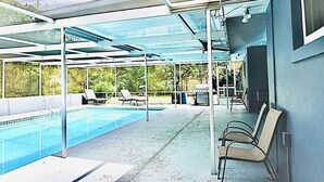 Un espace piscine extérieur abrité, équipé de chaises longues et d’un barbecue.