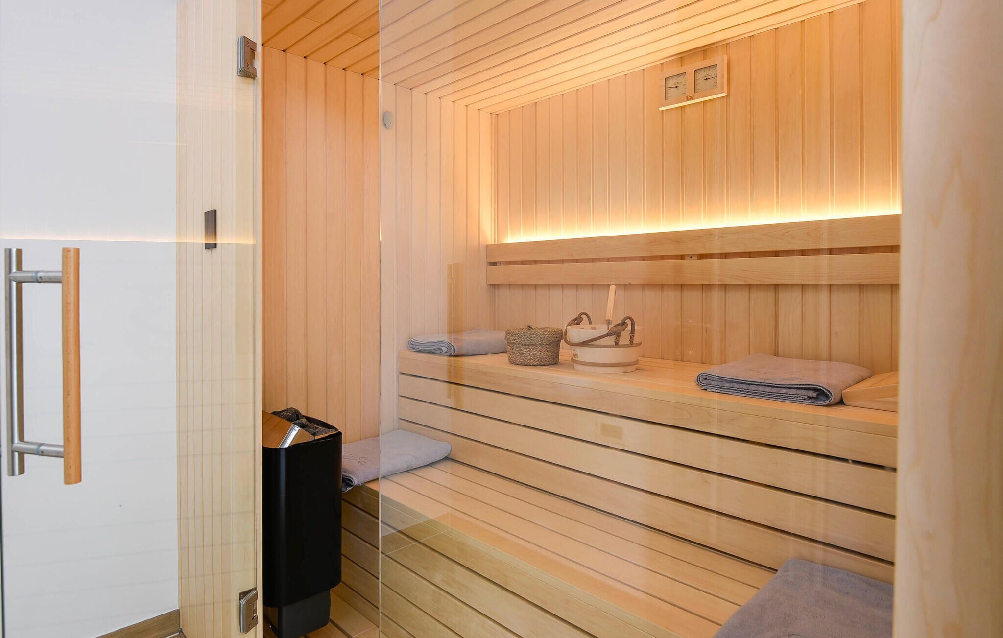 A sauna with wooden walls, a glass door, and a bench. There are towels and a basket on the bench.
