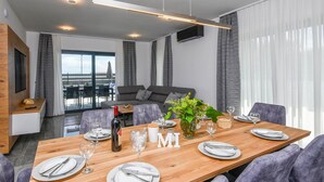 A modern dining area with a wooden table set for six, grey upholstered chairs, and a large window with curtains. - Pet friendly home in Orebic with sauna (Orebic)