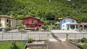 A row of two-story houses with balconies, set against a backdrop of lush green hills.