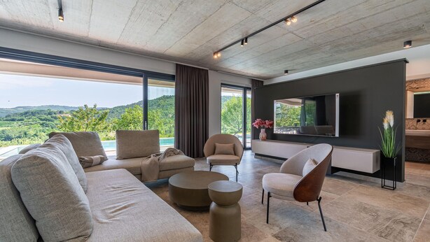 A modern living room with a large sofa, armchairs, a coffee table, and a flat-screen TV mounted on the wall.
