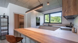 A modern kitchen with a wooden countertop, built-in oven, and a large window offering a view of greenery.