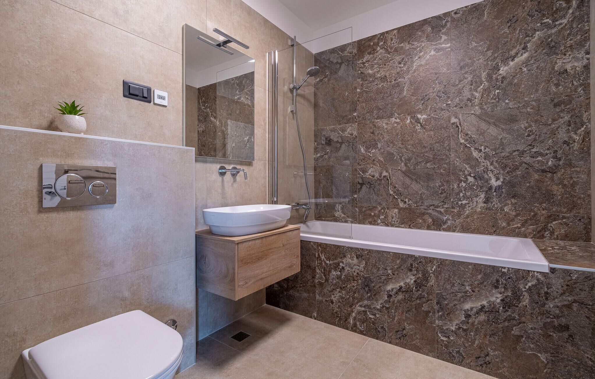 Un baño moderno con pared de mármol, una bañera independiente, un lavabo blanco y un inodoro.