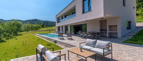 A modern two-story house with a pool, outdoor seating, and a kitchen area.