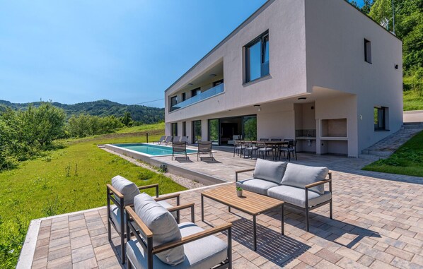 Une maison moderne à deux étages dotée d’une piscine, d’un espace extérieur aménagé et d’un coin cuisine.