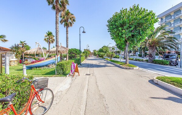 A street lined with palm trees, a bicycle, and a thatched-roof structure.