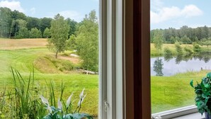 Blick aus einem Fenster auf ein Wiesfeld, einen kleinen Teich und einen bewaldeten Bereich.
