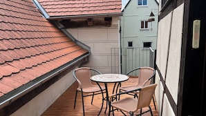 A wooden deck with a round table and four wicker chairs, a red-tiled roof, and a white building in the background. - old town residence (Weißenhorn)
