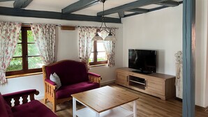 A living room with a wooden table, a red sofa, a TV, and a window with floral curtains. - old town residence (Weißenhorn)