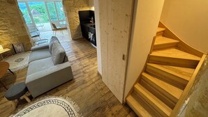 A modern interior with a stone wall, wooden flooring, a grey sofa, a dining area with chairs, and a staircase. - Bezenac grocery store (Castels et Bézenac)