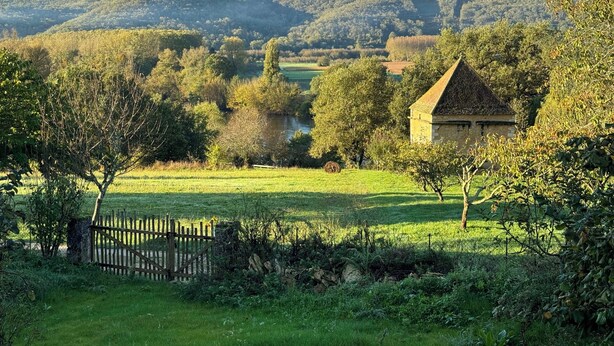 A rural landscape with a stone building, a river, and rolling hills in the background. - Bezenac grocery store (Castels et Bézenac)