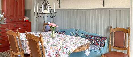 A dining area with a floral tablecloth, wooden chairs, a blue upholstered bench, and a chandelier.