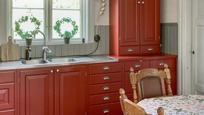 A kitchen with red cabinets, a wooden chair, and a window with two green wreaths. - 2 bedroom stunning home in Nås (Nås)