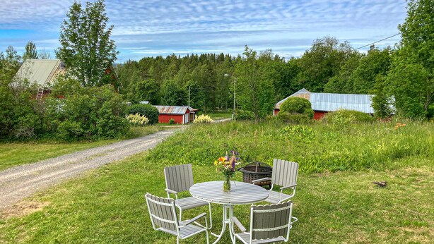 A rural setting with a gravel path leading to a round table with four chairs, surrounded by lush greenery and a small red building in the background. - 2 bedroom stunning home in Nås (Nås)
