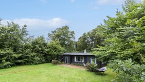 A small, dark-colored cabin with a single window and a chimney, surrounded by lush greenery and a well-maintained lawn. - 3 bedroom amazing home in Gilleleje (Gilleleje)