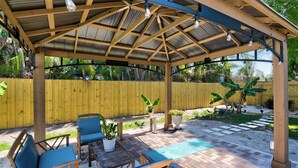 A covered patio area with seating, potted plants, and a pool.