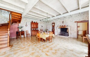 Un coin repas avec une table en bois dressée pour quatre personnes, entourée de chaises, d’un buffet en bois et d’une cheminée.