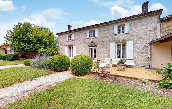 Une maison en pierre avec un patio dallé, des volets blancs et un jardin bien entretenu.