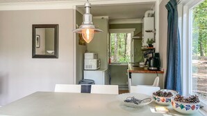 Un comedor con una mesa, sillas, una lámpara colgante y vista a la cocina a través de un vano abierto.