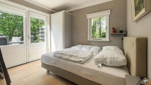 Un dormitorio con cama, ventana con vista a follaje y puerta corrediza a un balcón.