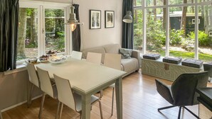Un comedor con una mesa, sillas y un sofá. Hay ventanas con cortinas, un radiador y cuadros en la pared.