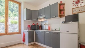 A modern kitchen with grey cabinets, a white refrigerator, and a window with a view of greenery. - Watering Can And Soldier (PLANAY)