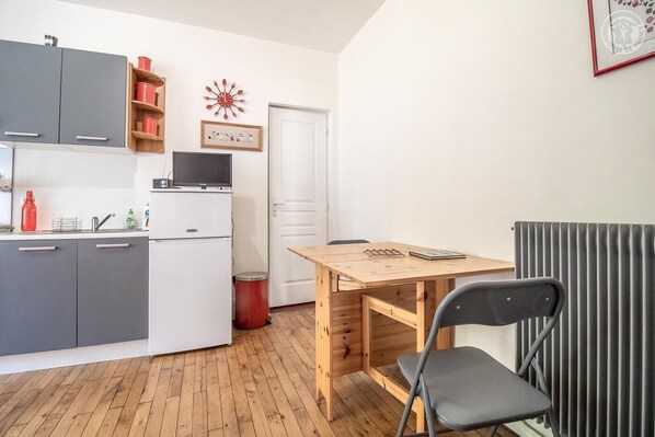 A compact kitchen with grey cabinets, a white refrigerator, and a wooden table with a chair.