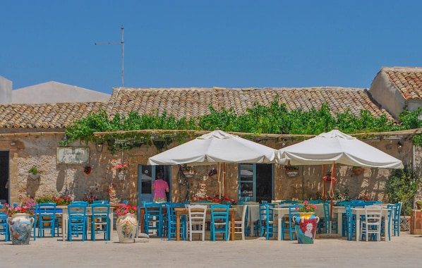 A traditional outdoor café with stone walls, tiled roofs, and blue chairs.