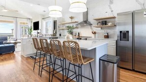 A modern kitchen with a central island, bar stools, stainless steel appliances, and pendant lighting. - Ocean Views-Private Heated Pool & Hot Tub-3 Kings! (Carolina Beach)