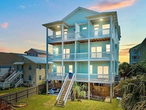 A multi-story building with balconies, a staircase, and a fenced yard.