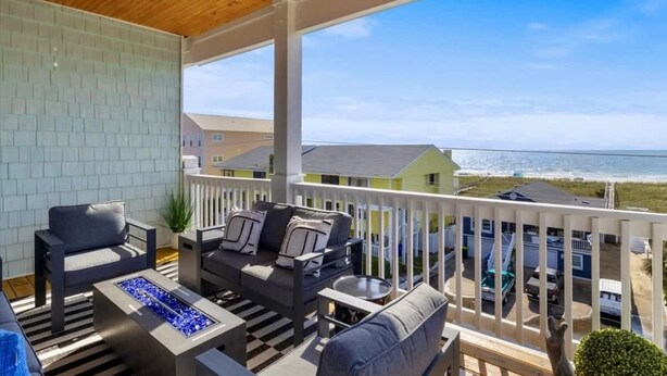 A covered outdoor seating area with a view of the ocean, a pool, and a building in the background. - Ocean Views-Private Heated Pool & Hot Tub-3 Kings! (Carolina Beach)