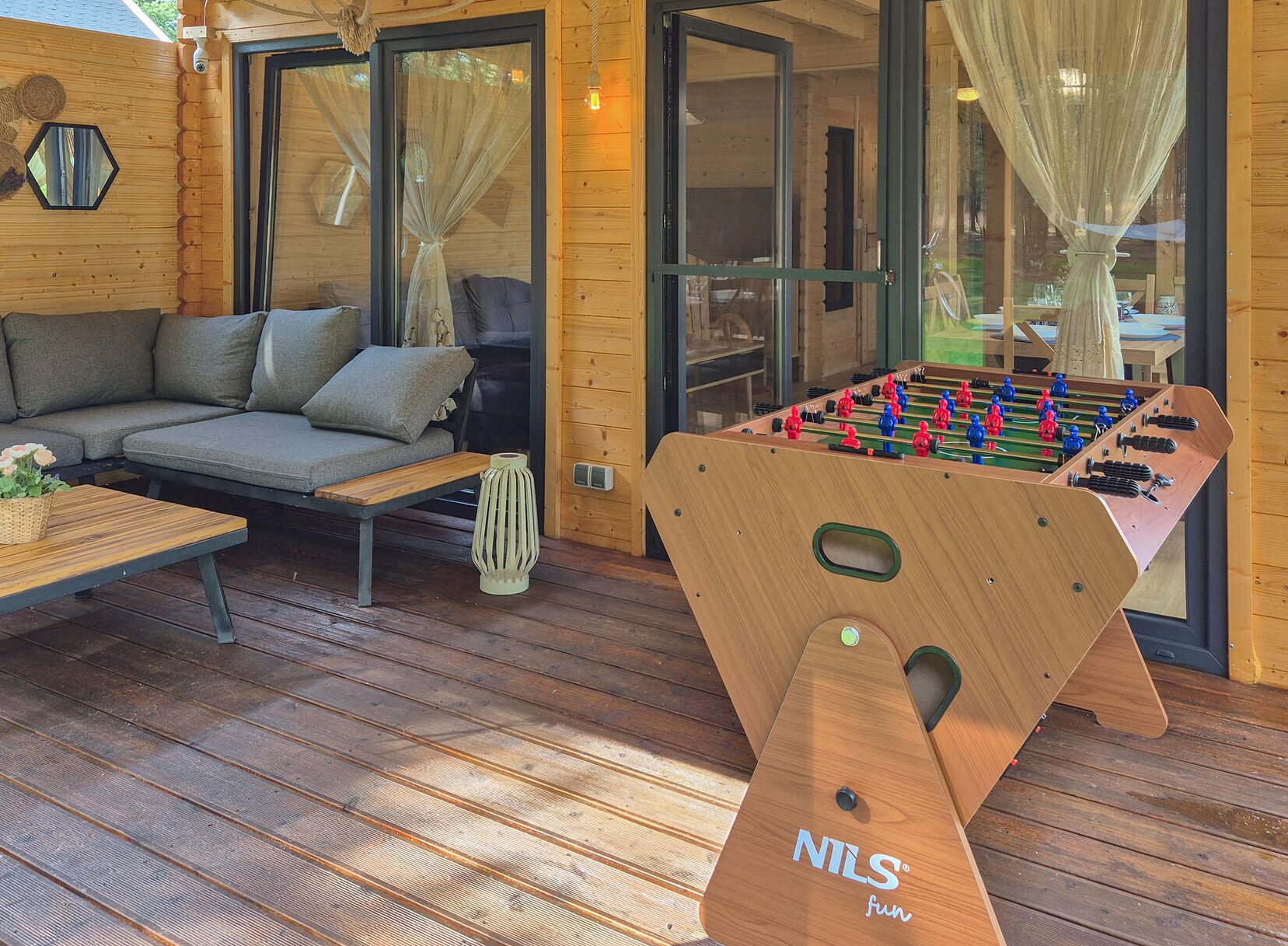 A cozy indoor space with a wooden sofa, a foosball table, and a large window with curtains.