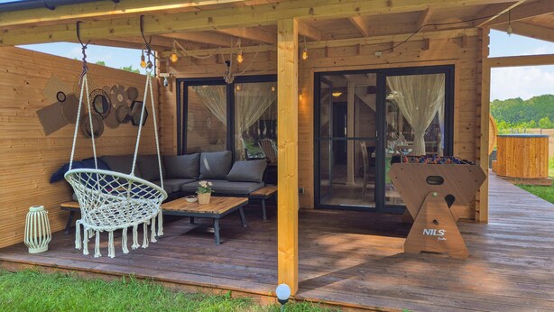 A wooden deck with a hanging chair, a sofa, and a foosball table.