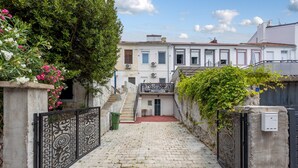 Une étroite entrée pavée de pierres mène à un bâtiment doté d’un portail en métal et d’un escalier qui aboutit à une porte.