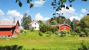 A rural landscape with a red barn, a white house, and a red house on a grassy hill.