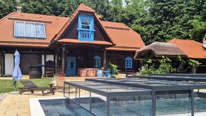 Una casa de madera tradicional con techo de tejas rojas, piscina y mobiliario exterior.