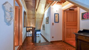 Un pasillo interior de madera con una escalera que conduce a una zona superior, puertas de madera y obras de arte enmarcadas en las paredes.
