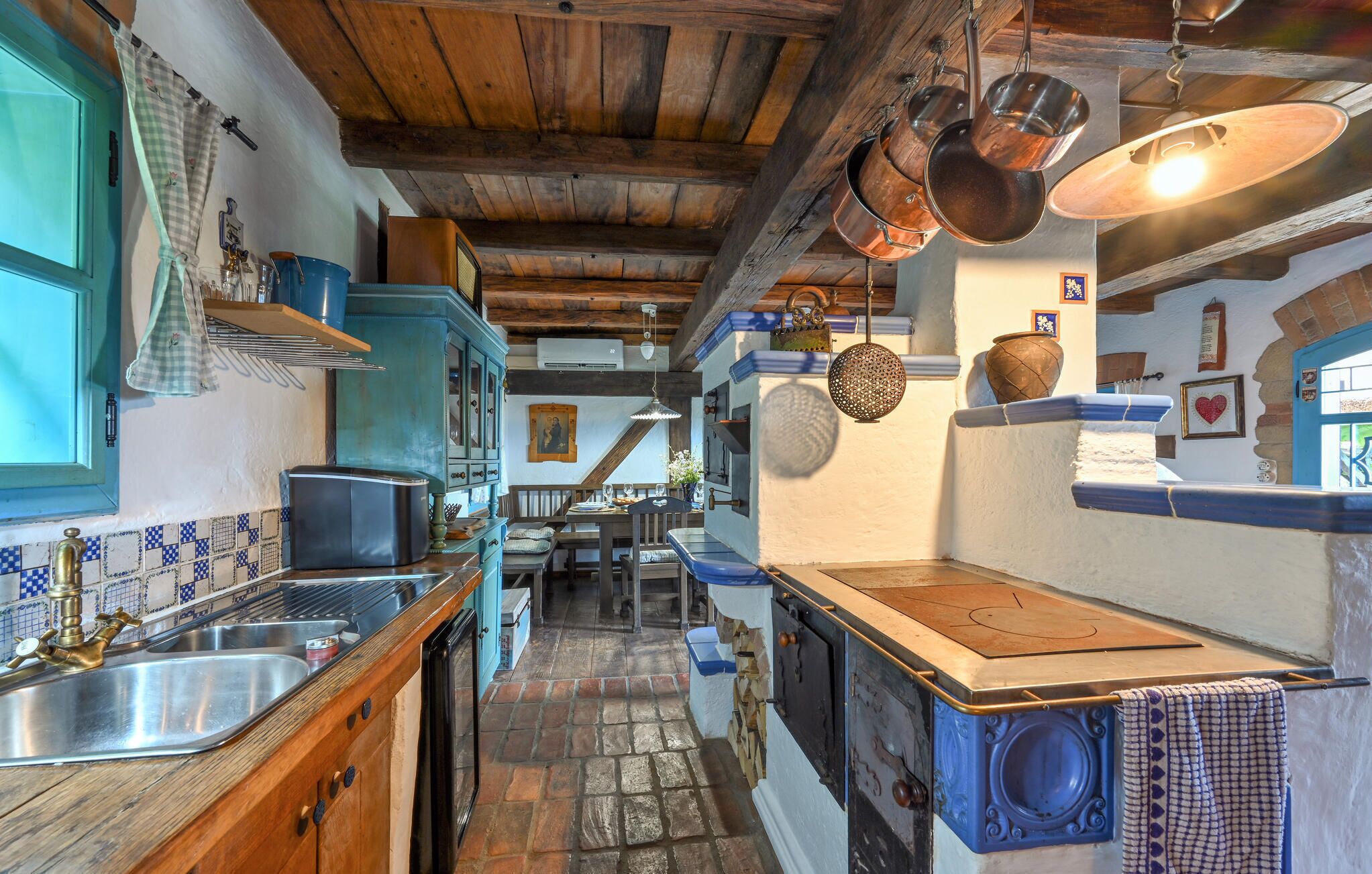 A rustic kitchen with wooden beams, a stone floor, and a traditional stove.